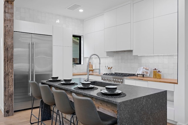 kitchen with light hardwood / wood-style floors, a kitchen bar, an island with sink, and appliances with stainless steel finishes