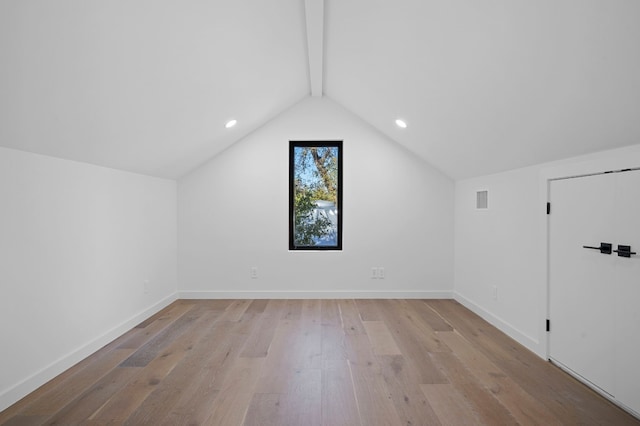 additional living space featuring light wood-type flooring and lofted ceiling with beams