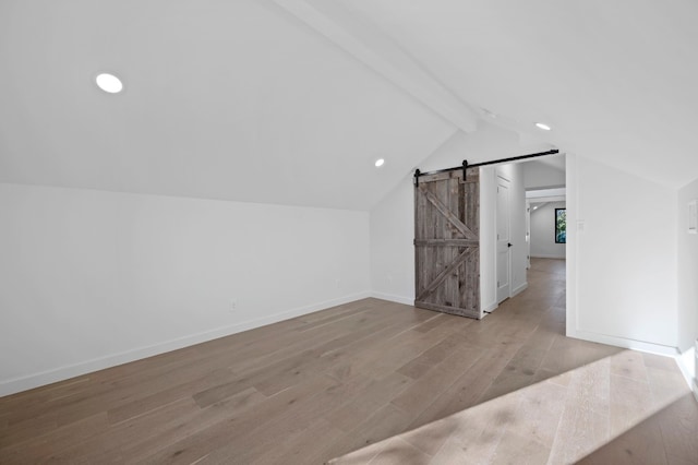 additional living space with light wood-type flooring, a barn door, and lofted ceiling with beams