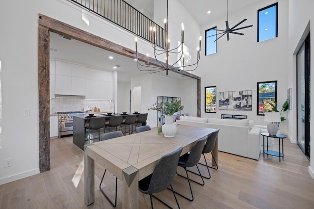 dining room with ceiling fan with notable chandelier, light hardwood / wood-style floors, sink, and a high ceiling