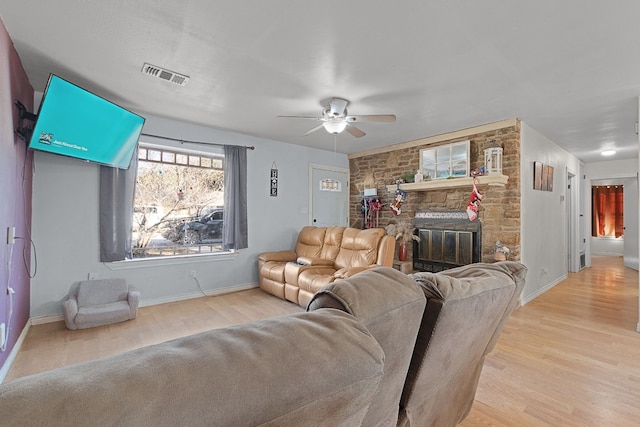 living room with light hardwood / wood-style flooring, ceiling fan, and a stone fireplace