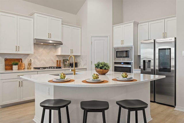 kitchen featuring appliances with stainless steel finishes, white cabinetry, a breakfast bar area, and an island with sink