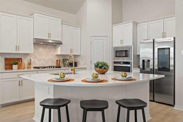 kitchen with appliances with stainless steel finishes, a center island with sink, white cabinets, and a kitchen breakfast bar