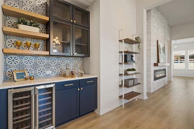 bar with a large fireplace, light hardwood / wood-style flooring, decorative backsplash, wine cooler, and blue cabinetry