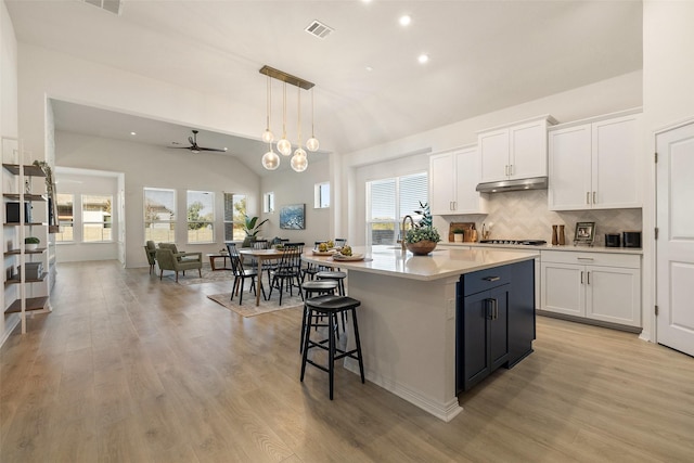 kitchen with decorative light fixtures, white cabinetry, ceiling fan, and a kitchen island with sink