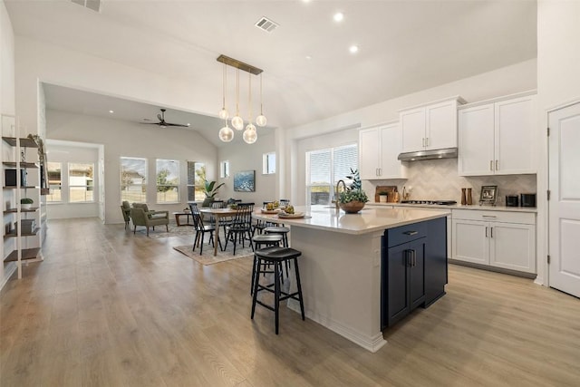 kitchen with decorative light fixtures, decorative backsplash, an island with sink, and white cabinets