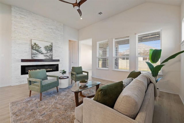 living room featuring vaulted ceiling, a fireplace, ceiling fan, and light hardwood / wood-style floors