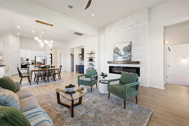 living room with ceiling fan, light hardwood / wood-style flooring, a towering ceiling, and a fireplace