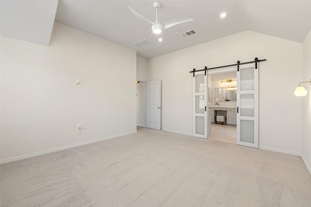 unfurnished bedroom with a barn door, light colored carpet, ceiling fan, ensuite bathroom, and lofted ceiling