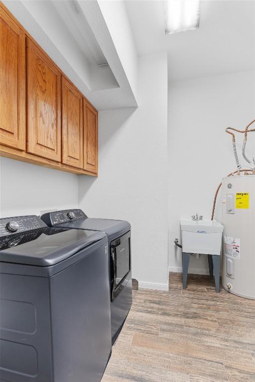 washroom featuring sink, cabinets, washing machine and dryer, water heater, and light hardwood / wood-style floors