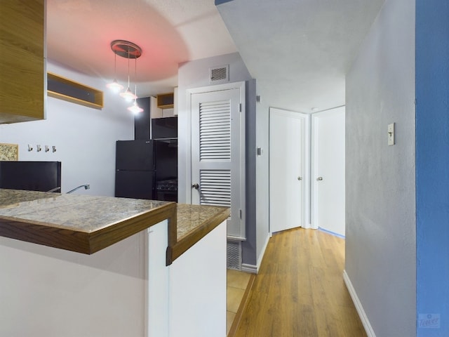 kitchen featuring kitchen peninsula, light wood-type flooring, black fridge, decorative light fixtures, and a breakfast bar area