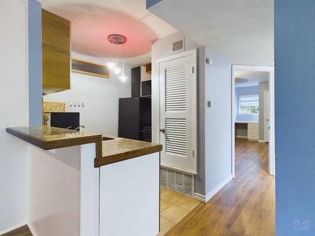 kitchen with black refrigerator, kitchen peninsula, sink, pendant lighting, and light hardwood / wood-style floors