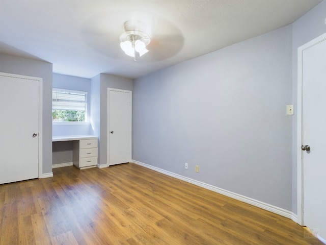 unfurnished bedroom featuring ceiling fan, hardwood / wood-style floors, and built in desk