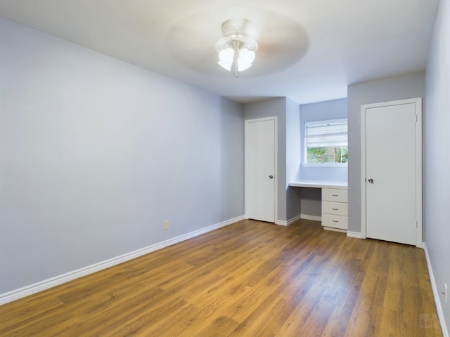 unfurnished bedroom with ceiling fan, built in desk, and dark hardwood / wood-style floors