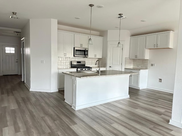 kitchen featuring stainless steel appliances, backsplash, an island with sink, white cabinets, and hardwood / wood-style flooring