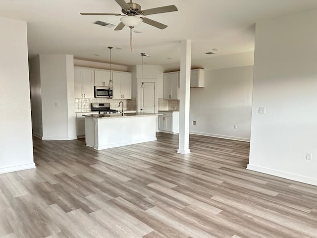 kitchen with a center island with sink, decorative light fixtures, light hardwood / wood-style floors, and appliances with stainless steel finishes