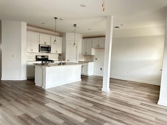 kitchen featuring appliances with stainless steel finishes, tasteful backsplash, light hardwood / wood-style flooring, and a kitchen island with sink