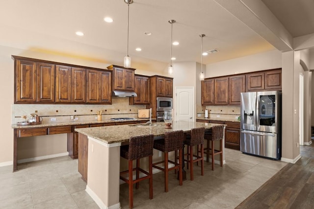 kitchen with hanging light fixtures, light stone counters, a center island with sink, and stainless steel appliances