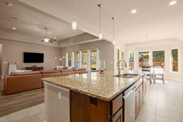 kitchen with dishwasher, a kitchen island with sink, sink, light wood-type flooring, and decorative light fixtures