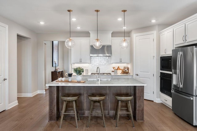 kitchen with black appliances, decorative light fixtures, a center island with sink, and white cabinets