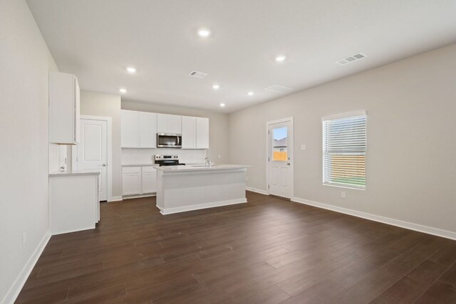 kitchen featuring appliances with stainless steel finishes, an island with sink, dark wood-style flooring, recessed lighting, and baseboards