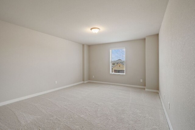 spare room featuring light carpet and baseboards