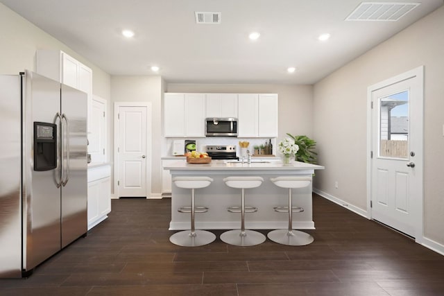 kitchen featuring stainless steel appliances, light countertops, dark wood-style floors, a kitchen breakfast bar, and recessed lighting