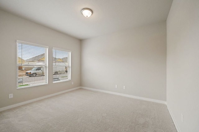 spare room featuring light colored carpet and baseboards