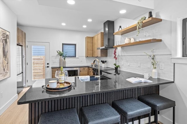 kitchen with a breakfast bar, decorative backsplash, light hardwood / wood-style floors, kitchen peninsula, and wall chimney range hood