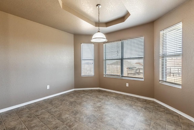 spare room featuring a textured ceiling, a tray ceiling, and a healthy amount of sunlight