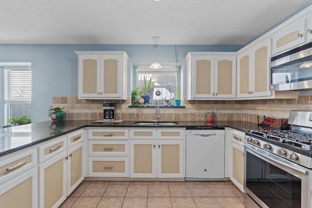 kitchen with sink, dark stone countertops, decorative backsplash, light tile patterned floors, and stainless steel appliances