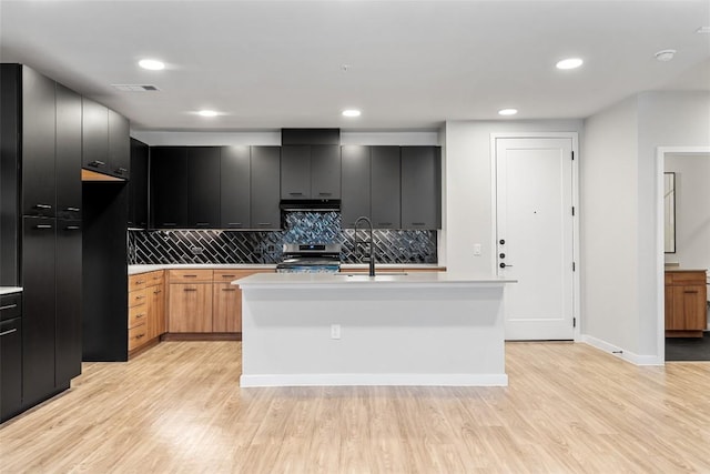 kitchen featuring backsplash, stainless steel stove, light hardwood / wood-style flooring, and a center island with sink