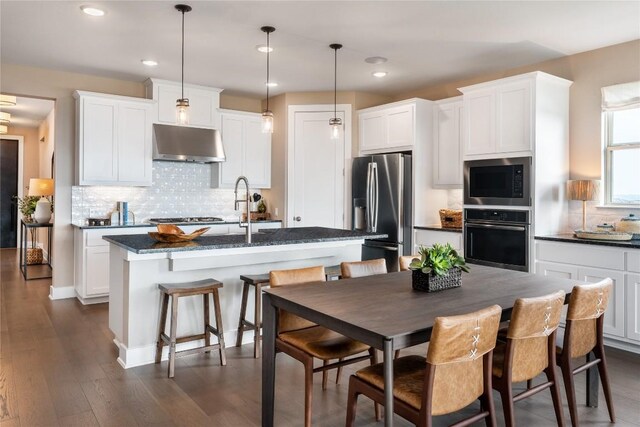 kitchen with pendant lighting, white cabinets, an island with sink, appliances with stainless steel finishes, and dark hardwood / wood-style flooring