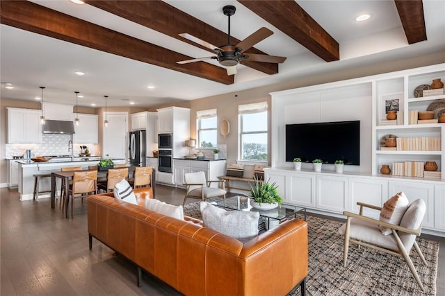 living room featuring ceiling fan, sink, beamed ceiling, and dark hardwood / wood-style floors