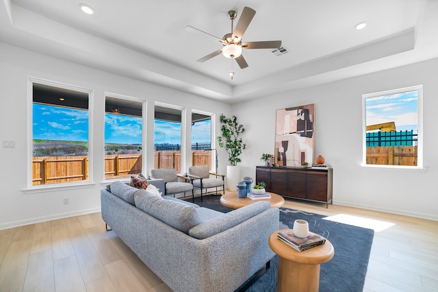 living area with visible vents, light wood-style flooring, baseboards, and a tray ceiling