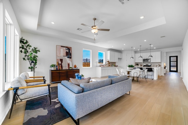 living room featuring recessed lighting, light wood-style flooring, a ceiling fan, and a tray ceiling