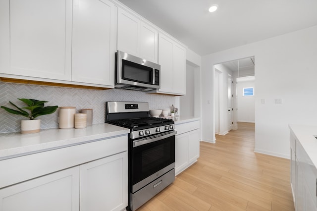 kitchen with light wood-style flooring, stainless steel appliances, light countertops, white cabinetry, and tasteful backsplash