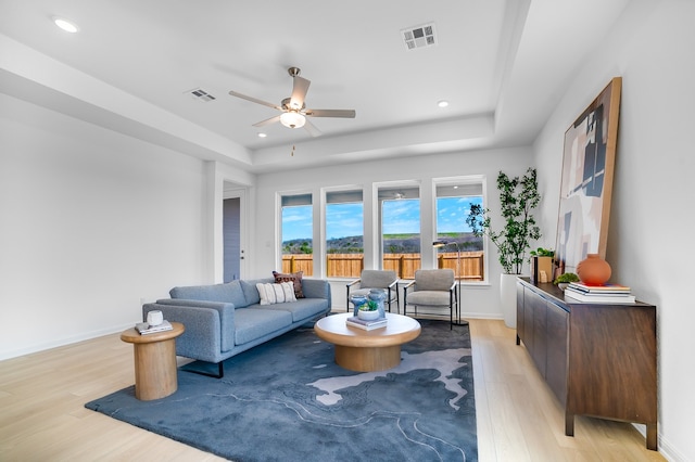 living area with visible vents, baseboards, a tray ceiling, light wood-style flooring, and ceiling fan