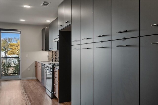 kitchen with decorative backsplash, gas stove, light hardwood / wood-style floors, and sink