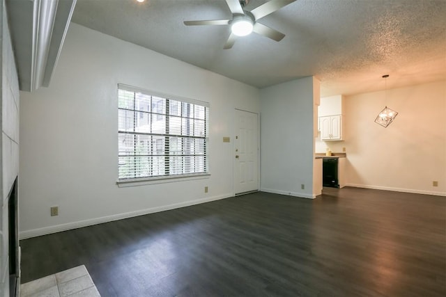 unfurnished living room with a textured ceiling, dark wood-type flooring, and ceiling fan with notable chandelier