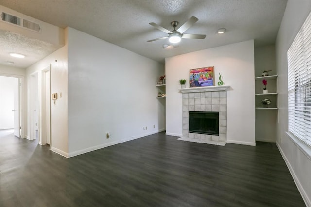 unfurnished living room with a textured ceiling, ceiling fan, dark wood-type flooring, and a tiled fireplace