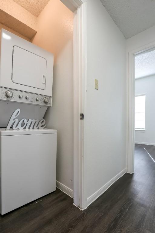 clothes washing area with stacked washer / dryer, dark hardwood / wood-style flooring, and a textured ceiling