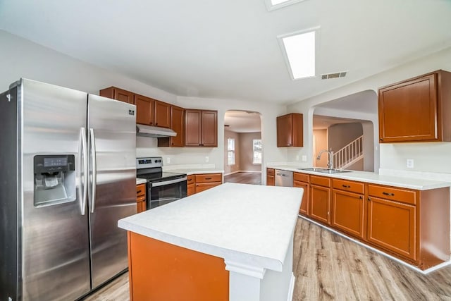 kitchen with sink, light hardwood / wood-style flooring, kitchen peninsula, a kitchen island, and appliances with stainless steel finishes