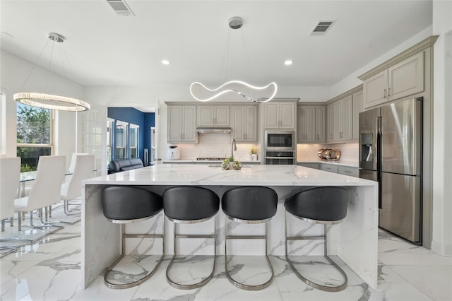 kitchen with pendant lighting, appliances with stainless steel finishes, tasteful backsplash, a kitchen island, and light stone counters