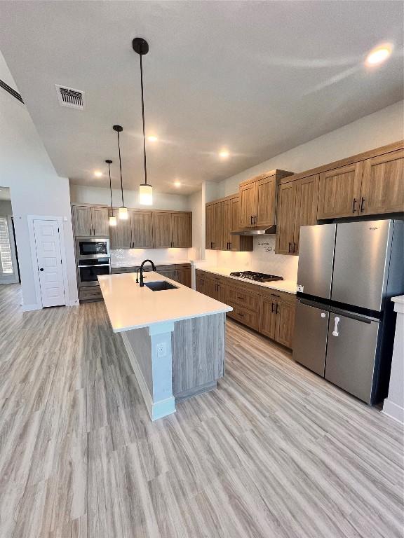 kitchen featuring light wood-type flooring, stainless steel appliances, sink, pendant lighting, and a center island with sink