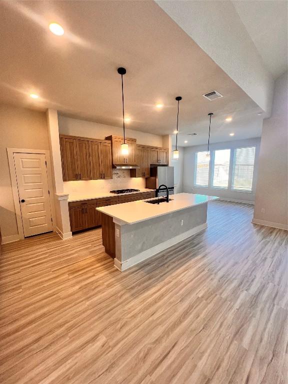 kitchen featuring stainless steel refrigerator, light hardwood / wood-style flooring, hanging light fixtures, and a spacious island