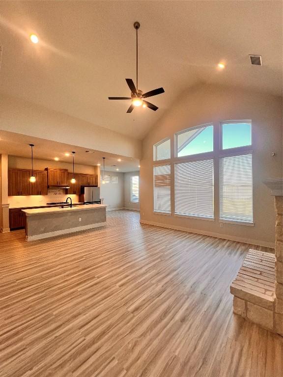 unfurnished living room with a stone fireplace, sink, vaulted ceiling, ceiling fan, and light wood-type flooring