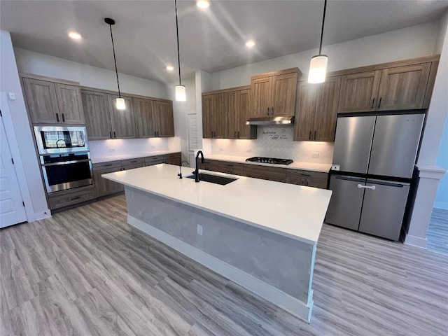 kitchen featuring a kitchen island with sink, sink, hanging light fixtures, light wood-type flooring, and stainless steel appliances