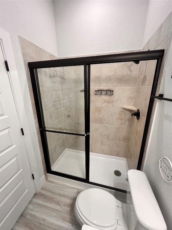 bathroom with toilet, a shower with door, and wood-type flooring