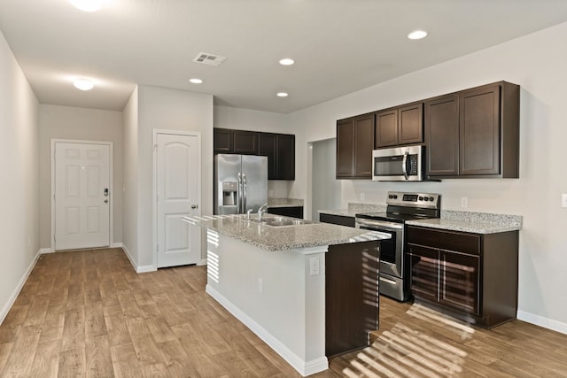 kitchen with sink, an island with sink, dark brown cabinets, light hardwood / wood-style floors, and stainless steel appliances